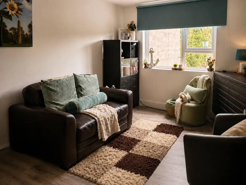 A bright therapy room with a leather sofa, soft cushions and throws, and a window looking onto greenery